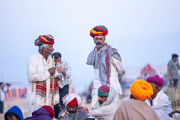 Pushkar, Rajasthan, India - November 2024: Group of a rajasthani male in traditional white clothes with colourful turban at desert ground in winter morning with camel during pushkar fair.