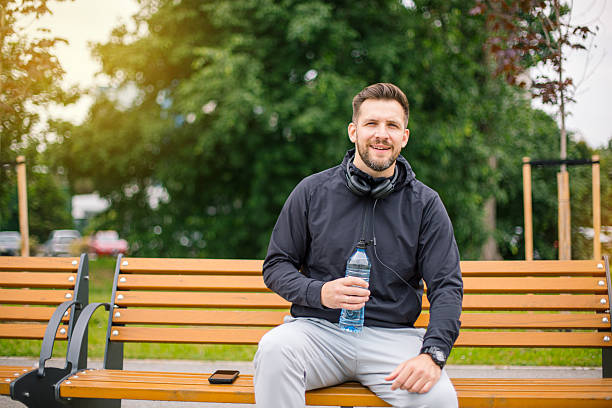 istock Smiling sportsman resting on bench and drinking water after training 2219813428