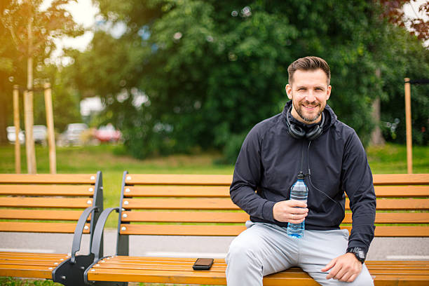 istock Smiling sportsman resting on bench and drinking water after training 2219813576