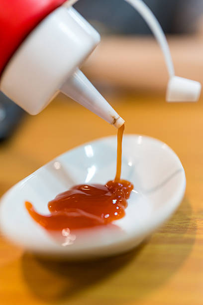 istock Person squeezing ketchup from bottle dispenser onto a pristine white plate. 2219817466