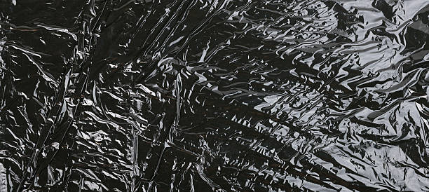 Textured black crumpled plastic film that reflects light artistically.