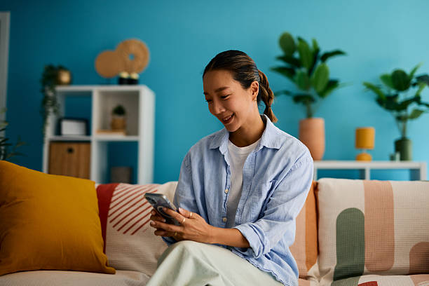 istock Young Asian woman using mobile phone while relaxing on sofa at home 2219826739