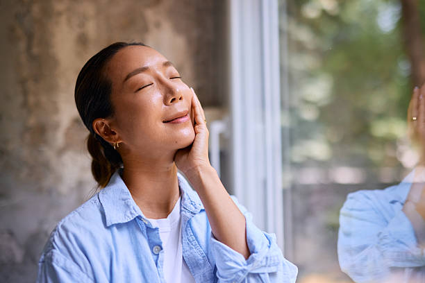 istock Young woman touching her face and enjoying sunlight from window 2219827160