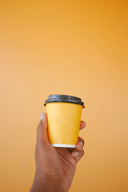 istock Bright yellow coffee cup held against a vibrant orange background 2219828194