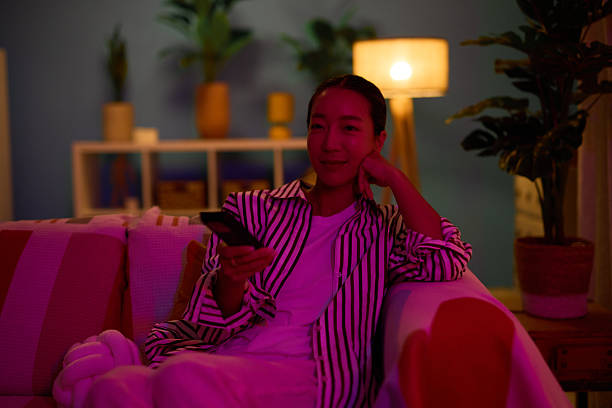 istock Young woman relaxing on sofa watching television, holding remote control 2219828265