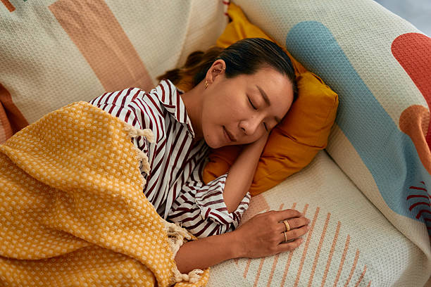 暖かい毛布に覆われた快適なソファで安らかに眠っている若い女性 - 睡眠 ストックフォトと画像