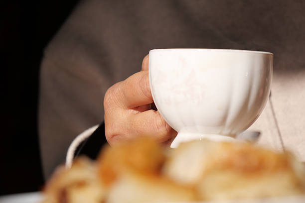 A person holds a fine porcelain cup while enjoying baked goods.