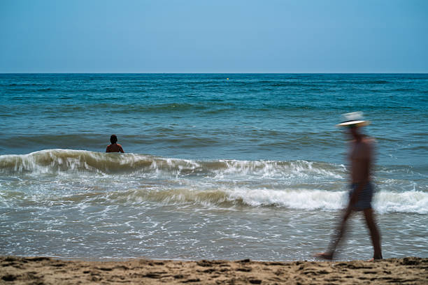 Visitors enjoy a sunny day at Isla Canela beach, with one person swimming in the sea while another strolls along the sandy shore.