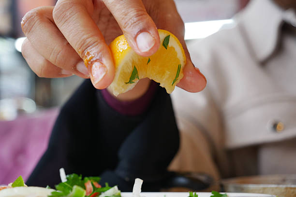 A hand is squeezing fresh lemon juice onto a colorful dish filled with herbs.