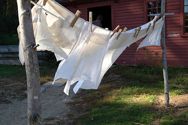 White cloths hanging on antique clothesline held by clothespins blowing in the wind in front of red wood house