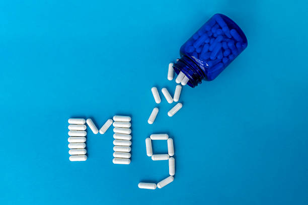 istock Blue bottle with white magnesium tablets that are spilling out and tablets lined with the Mg symbol on a blue medical background with space for text. Dietary supplements. 2219835732