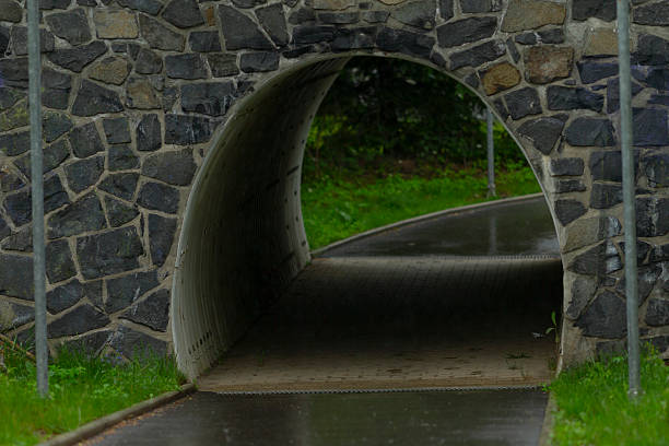 A picturesque pathway winds through an enchanting stone archway, surrounded by lush grass and greenery, creating a serene space perfect for relaxation and enjoying the landscape