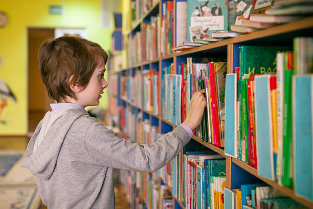 istock 8-year-old boy with brown hair choosing book in library. 2219842600