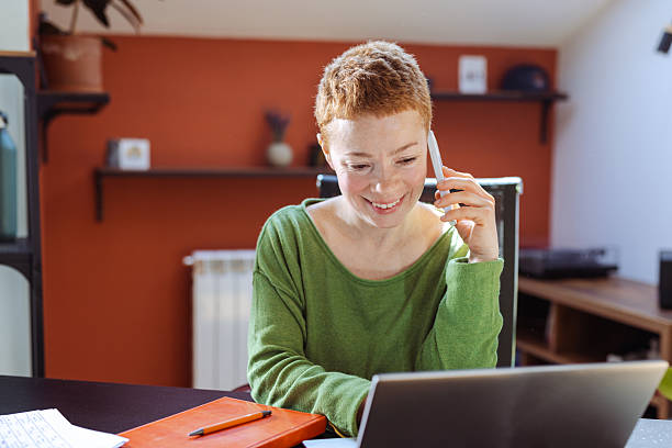 istock Smiling woman working on her laptop while having a phone conversation 2219846462