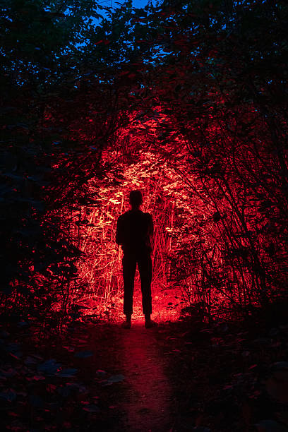 Dark silhouette of a man on the path and red light from a flashlight. Night Horror forest scene creates a scary and creepy feeling