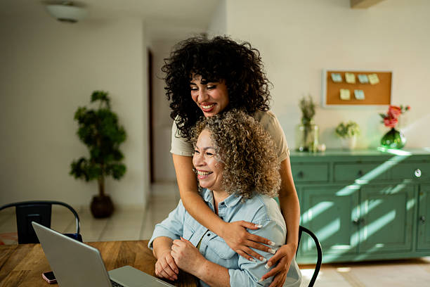 istock Young daughter embracing mother while she using laptop at home 2219857966