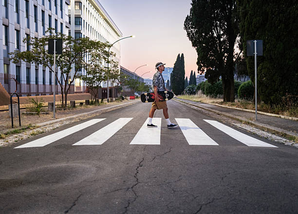 istock Young Man Skateboarding Through City Crosswalk at Sunset 2219858047