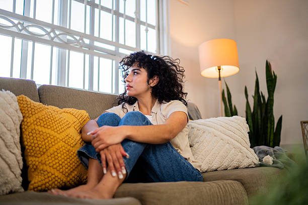 Sad young woman looking through the window at home