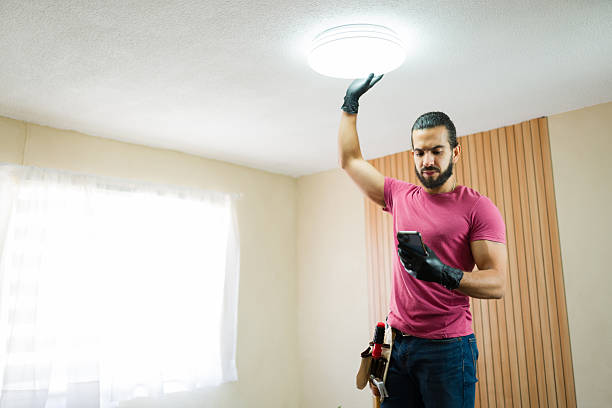 istock Male electrician installing ceiling light fixture while pairing it with a smartphone in a smart home 2219863499
