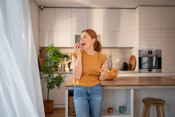 istock Young woman enjoying a peach in her modern kitchen 2219864104