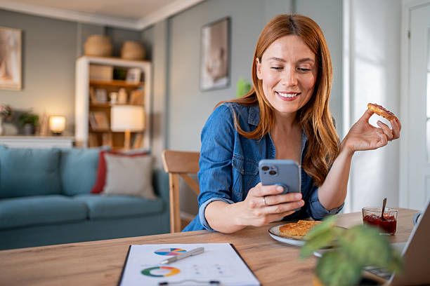 istock Smiling freelancer woman using mobile phone and eating breakfast at home 2219864209