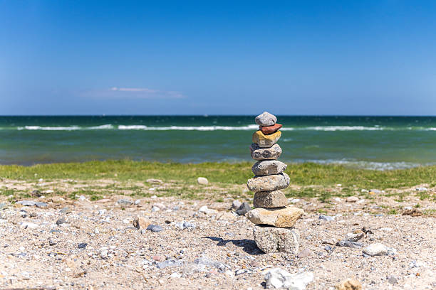 Pebble tower standing on a sandy beach with green grass and the ocean in the background, symbolizing balance, peace, and mindfulness