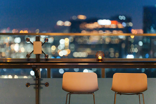 istock Night city view from a rooftop bar with two empty chairs facing the skyline and a candle on the glass railing. 2219868686