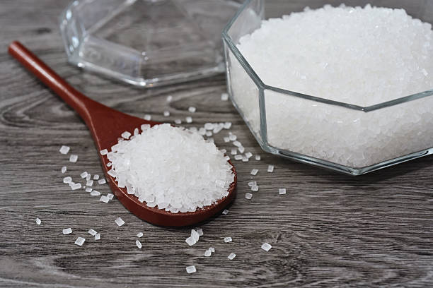 istock Crystal sugar on wooden spoon with white granulated sugar bottles background. 2219871168
