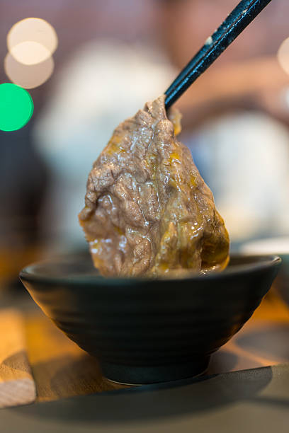 Using black chopsticks dip meat in to raw egg. Eating sukiyaki