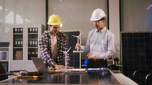 istock Two Asian businessmen wearing engineer hats table, discussing solar panels and wind turbines. They plan environmental projects, focusing on solar energy solutions and renewable energy installations 2219882805