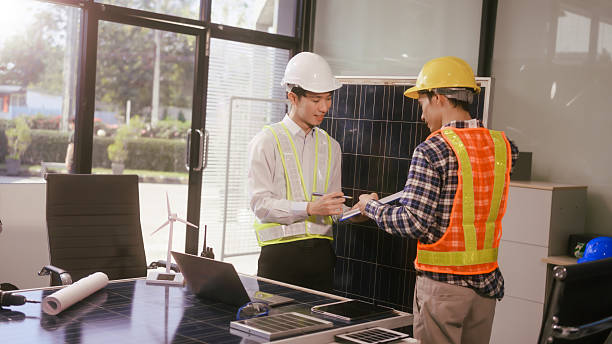 istock Two Asian businessmen wearing engineer hats table, discussing solar panels and wind turbines. They plan environmental projects, focusing on solar energy solutions and renewable energy installations 2219882836