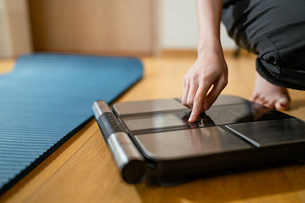 Woman syncing her smartphone with a weighing scale, setting it up to track her progress for new year to achieve new fitness goals, stay healthy, and embrace a balanced lifestyle