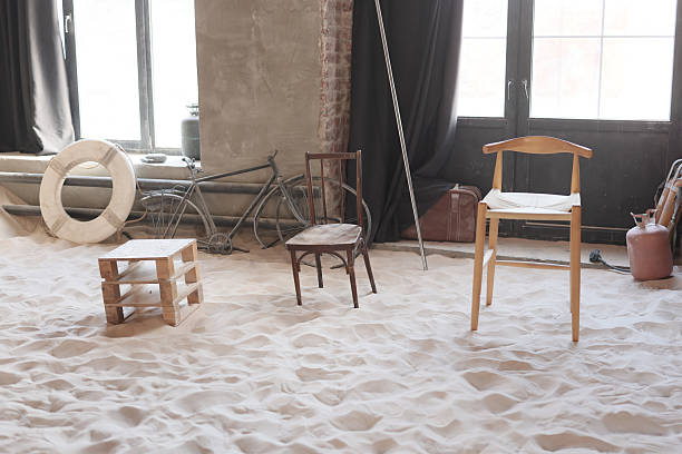 An artistic setup showcases a diverse array of chairs arranged thoughtfully on a sandy surface indoors