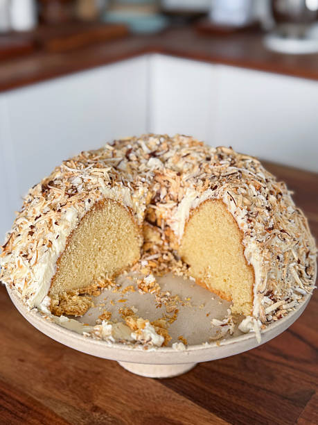 Image of coconut sponge cake, butter icing, roasted flakes on cake stand in bundt ring tin /  homemade dessert, creamy topping