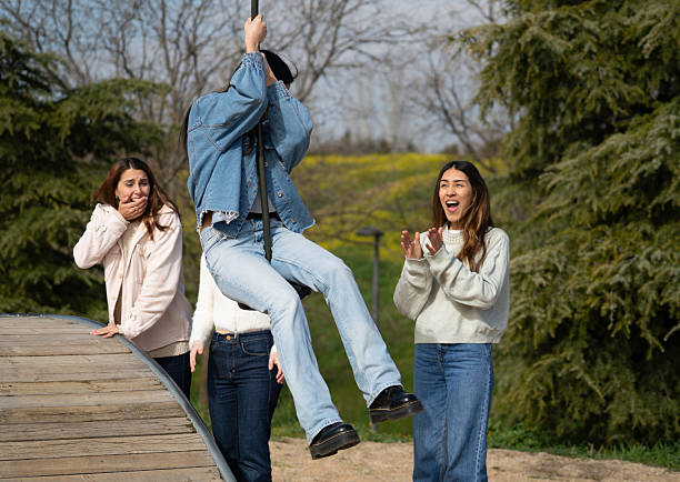 Three young adult women enjoying a sunny day at the park, one swinging high while her friends watch and cheer