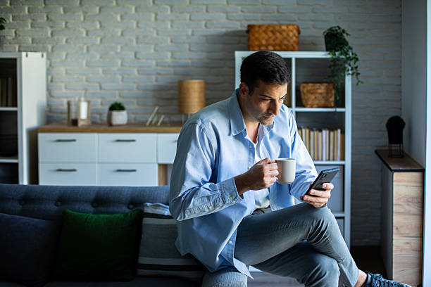 istock Casual Man Browsing Phone and Drinking Coffee by Window 2219904328