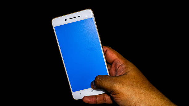 istock White and gold smartphone held in one hand over black background, blue screen ready for UI editing or mockup template, modern tech scene for creative projects 2219906211