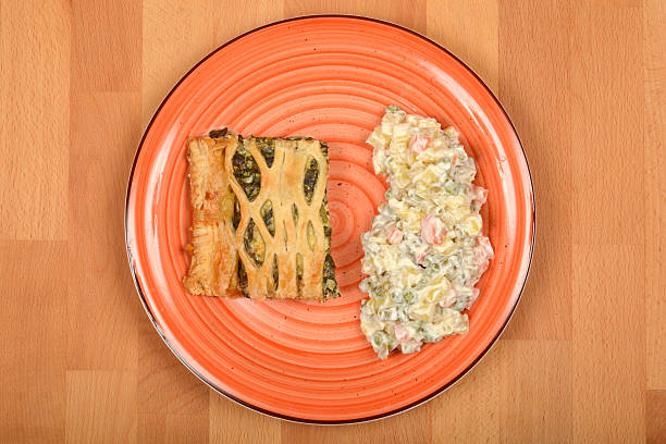 A top-down view shows a slice of spinach and cheese puff pastry served with Croatian-style French salad on an orange plate