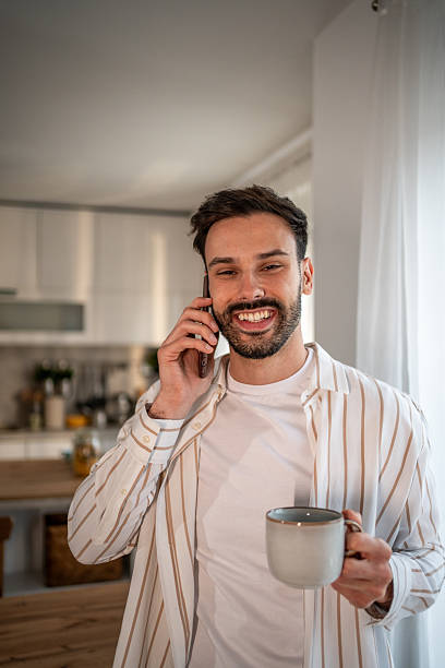 istock Young man talking on the phone and drinking coffee in his kitchen 2219911421