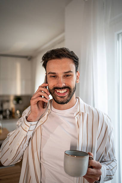 istock Young man talking on smartphone and drinking coffee at home 2219911424