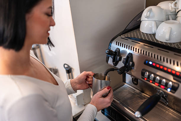 istock Young Female Barista Skillfully Foaming Milk at Modern Coffee Machine in Cozy Caf? Setting 2219913949