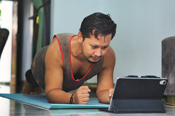 istock Man Performing Plank Exercise While Watching Online Workout on Tablet at Home 2219915178