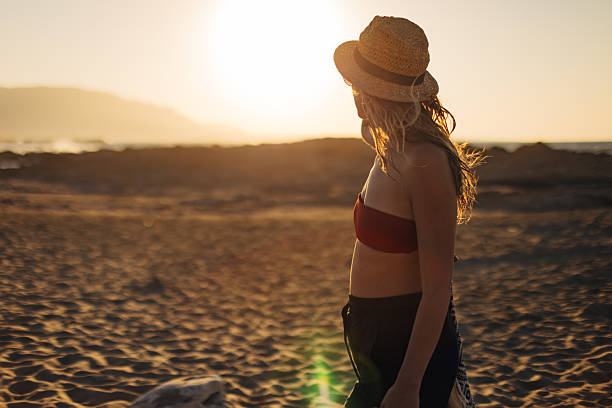 A woman in bikini top and summer short walks on a sandy  beach after a whole day of swimming and sunbathing
