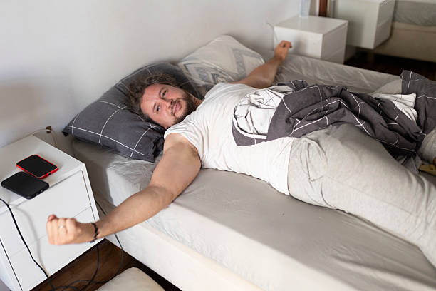 istock Young man waking up and stretching in bed after sleeping 2219915573