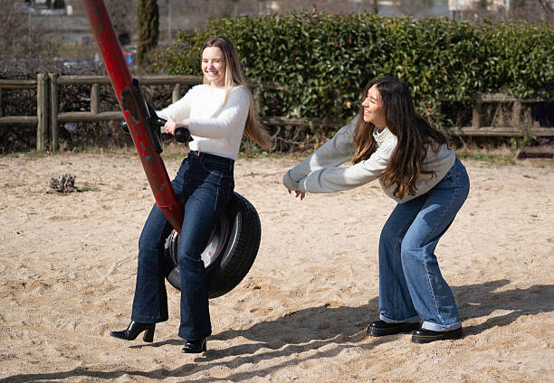 Two young women enjoying a playful moment on a playground swing, spinning and laughing together