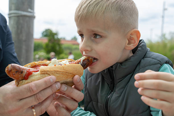 istock Young Boy Enjoying a Hot Dog Outdoors with Enthusiasm 2219916501