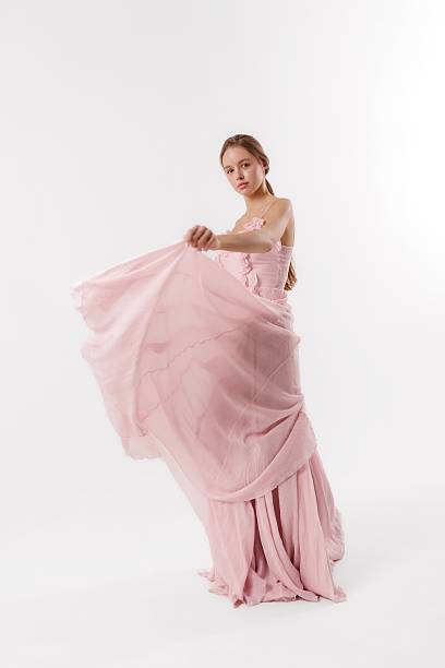 istock Elegant woman in flowing pink dress poses in a minimalist studio setting while creating a dynamic motion 2219928238