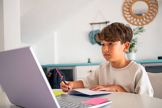 istock Child engaged in online learning while taking notes at home on a sunny day 2219929383