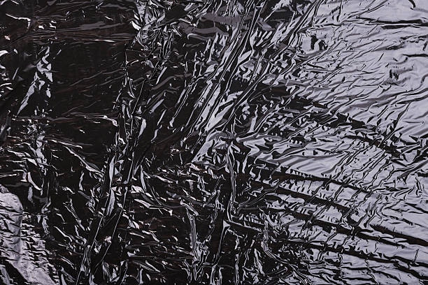 Textured black crumpled plastic film that reflects light artistically.