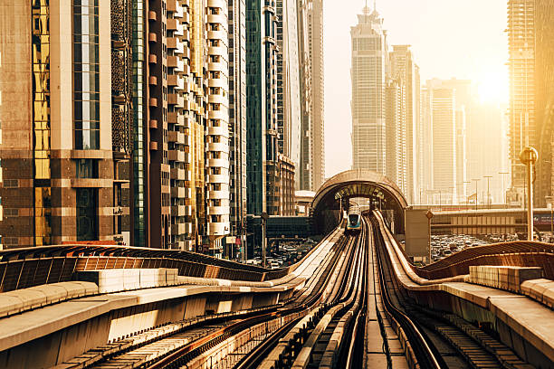 Elevated view of Sheikh Zayed Road in Dubai, showcasing tall modern skyscrapers, metro track, and dynamic urban architecture under the golden sunlight.